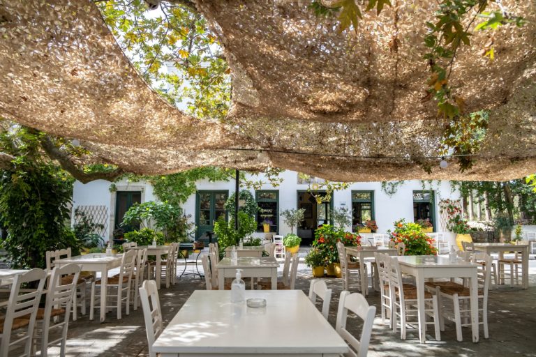 Greek tavern with table and chair under net at Kithira island Milopotamos. Pots with flowers.